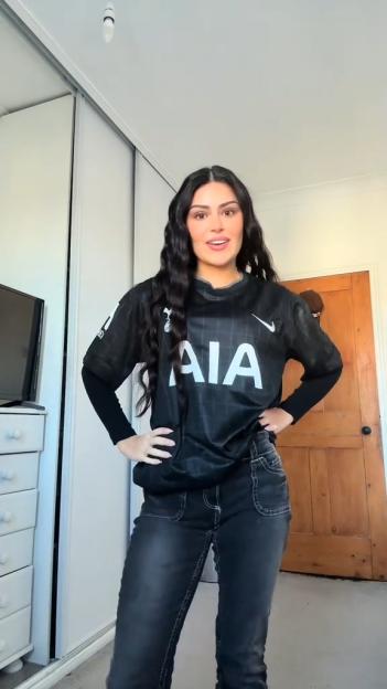 Woman posing in a black Tottenham Hotspurs soccer jersey and black jeans.