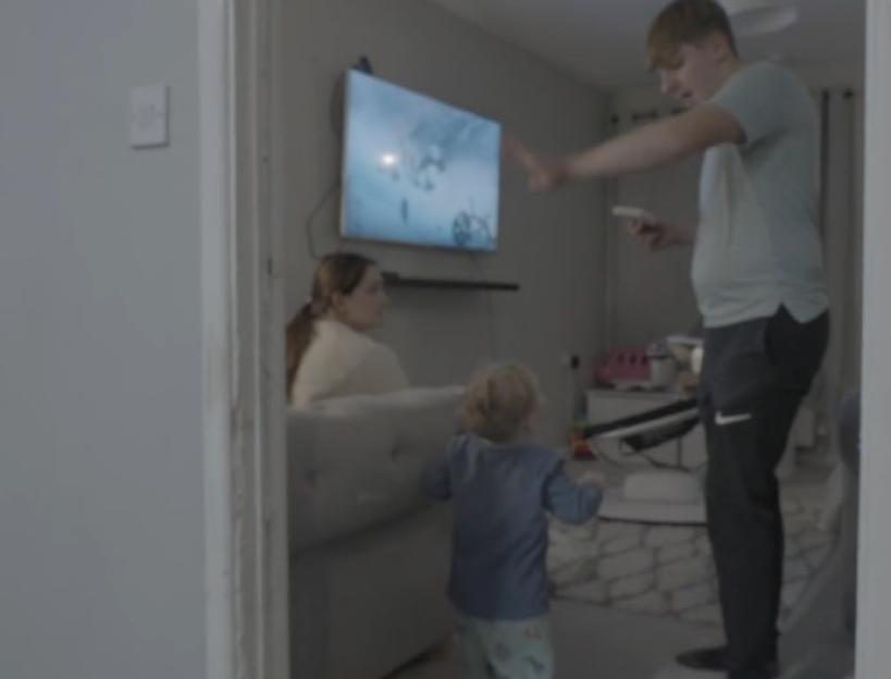 Man, woman, and child in a living room with a TV showing a snowy scene.