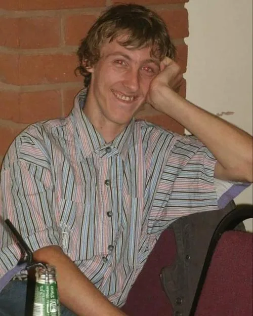 Photo of Rubin Blount, a man with light brown, curly hair, wearing a striped shirt, smiling and leaning his head on his hand.