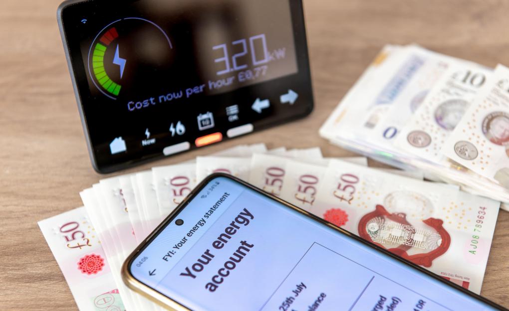A mobile phone displaying an energy bill, a smart energy meter, and British banknotes.