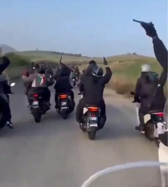 Men on scooters with guns raised in the air.