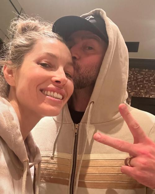 Jessica Biel smiling at the camera as Justin Timberlake kisses her temple, making a peace sign.
