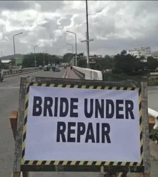 A sign in front of a bridge reads "BRIDE UNDER REPAIR" with a warning stripe around its edge.