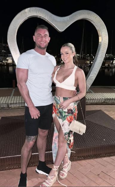 Sam and Abigail Garside posing in front of a metal heart sculpture at night.