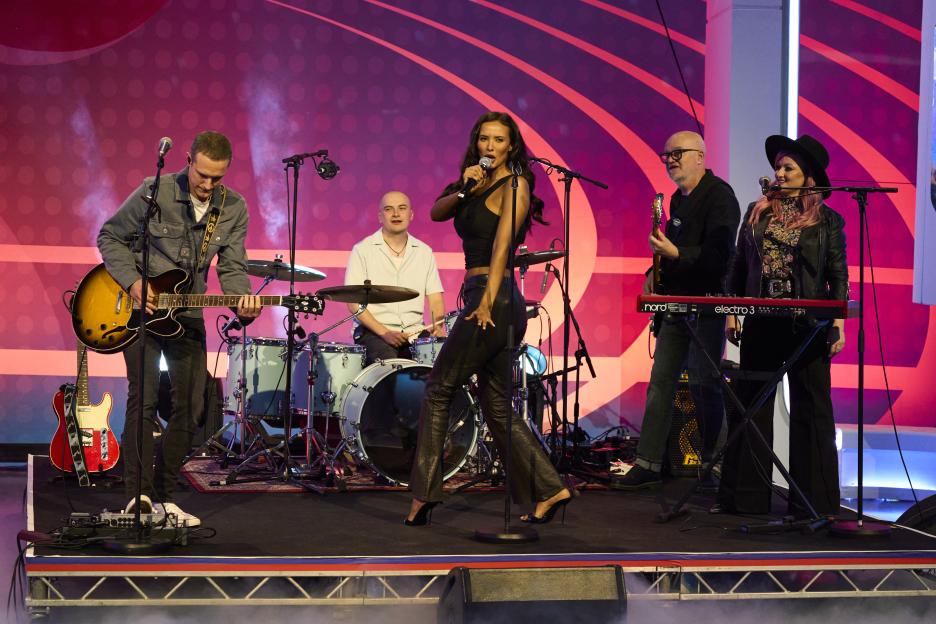 Maya Jama performing "Arctic Monkeys" with a live band.