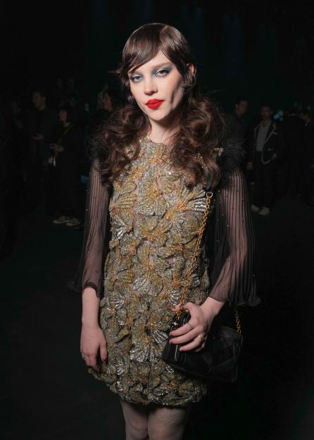 Sophie Thatcher wearing a sparkling gold and silver dress with sheer black sleeves and a small black purse.