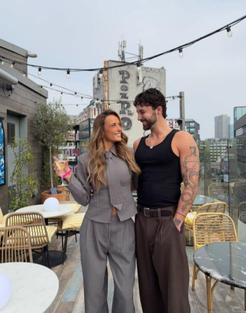 Millie Court and Zac look at each other on a rooftop bar.
