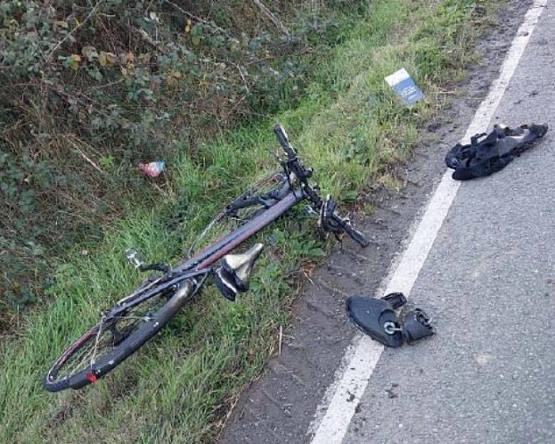 A bicycle lying in grass beside a road with a broken bike shoe.