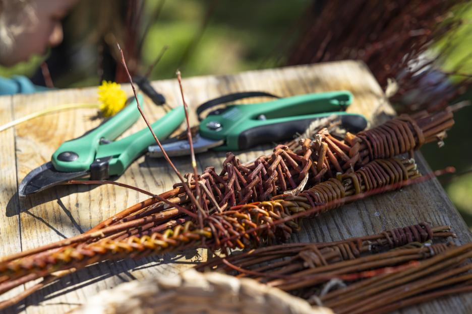 Pruners and bundles of woven willow branches on a wooden table.