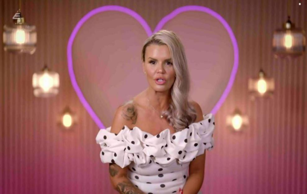 Kerry Katona looking frustrated while wearing a white polka dot dress.