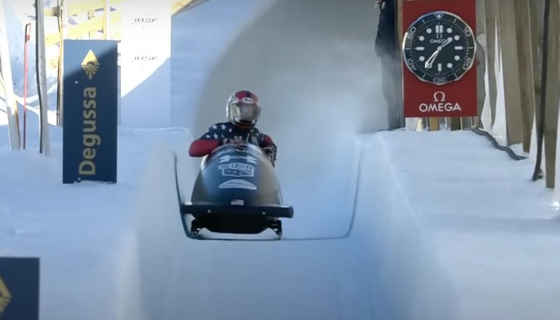 A bobsledder in a USA-themed suit and helmet navigates a snowy track.