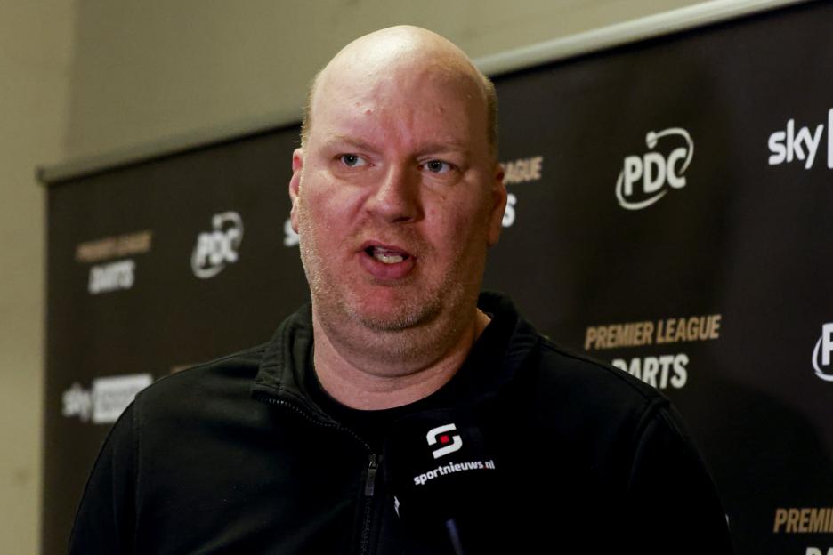A man in a black jacket speaking at a press conference for the Premier League Darts.