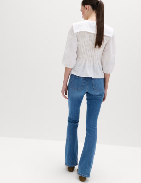 A model from the back, wearing a white smocked peasant blouse with a large collar and wide-leg denim jeans.