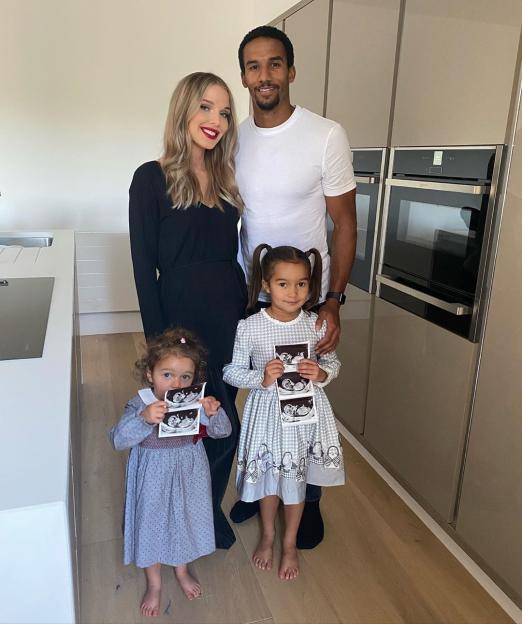 Family portrait of a couple and two young daughters, one of whom is holding ultrasound images.