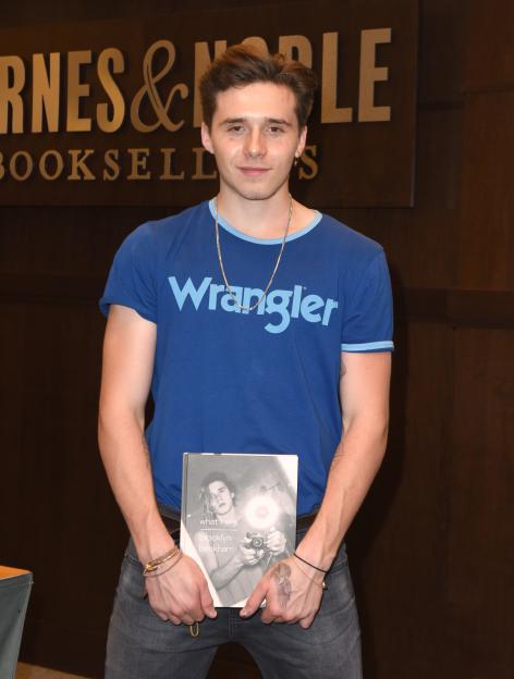 Brooklyn Beckham in a blue Wrangler t-shirt holds his new book "What I See" at a book signing.