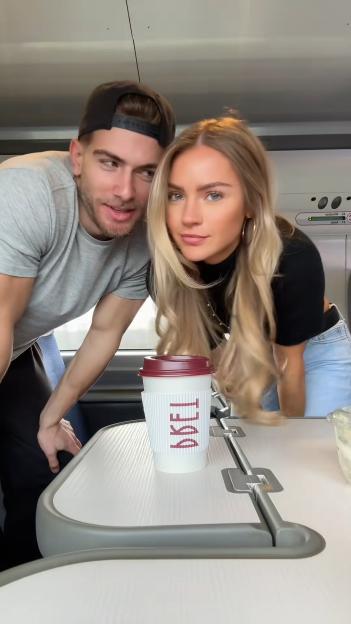 Livvy and Joel Evans posing for a photo with a coffee cup in front of them on a train.
