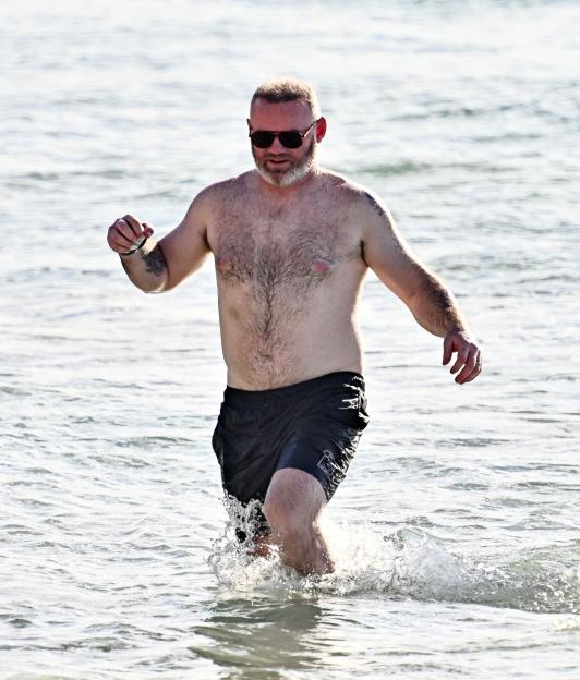 Former England footballer Wayne Rooney walks through the water on a beach in Barbados.