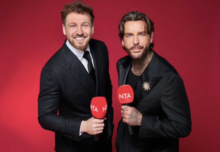 Two men in suits hold red microphones with "NTA" on them against a red background.