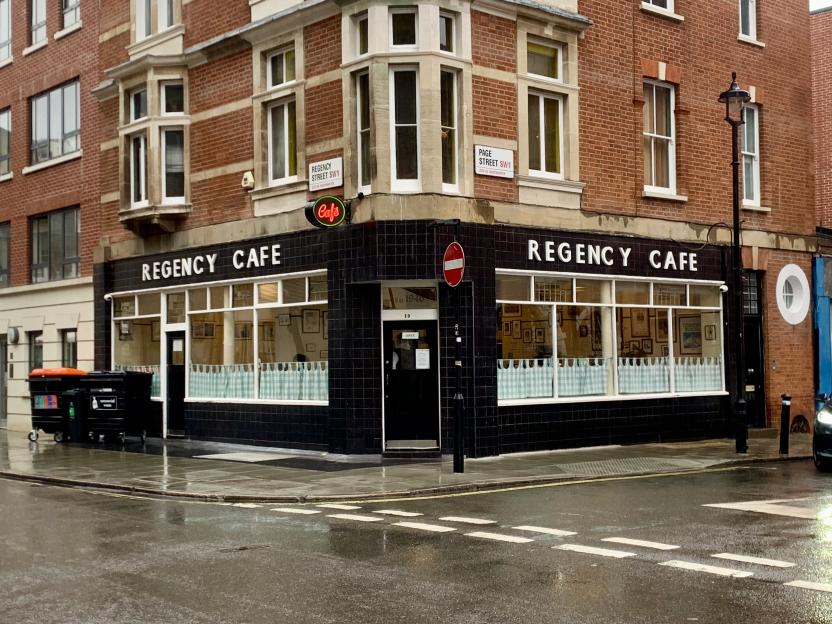 A corner building on a wet street with a cafe on the ground floor, street signs indicate Regency Street and Page Street.