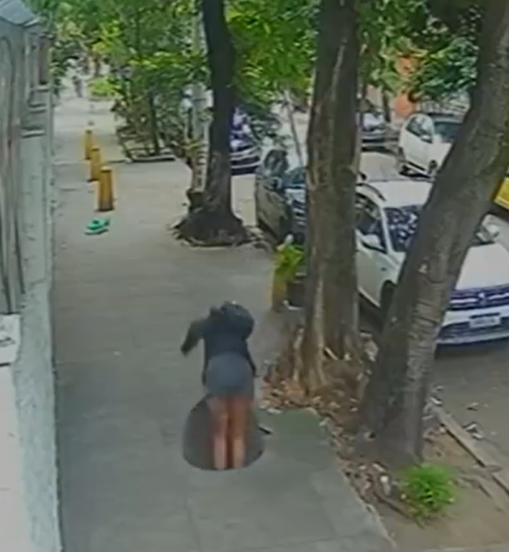 A person falling into an open manhole on a sidewalk.