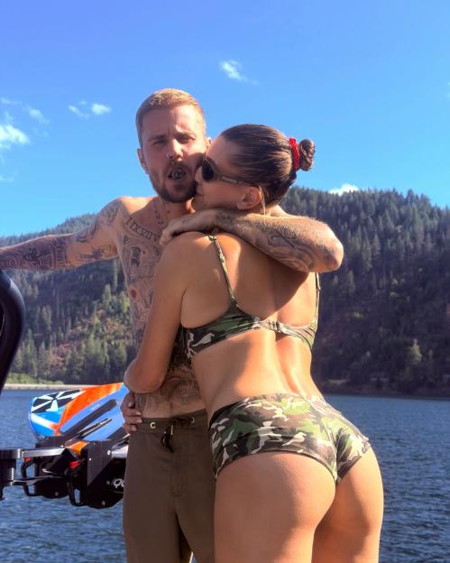 A man with tattoos embracing a woman in camouflage swimwear while on a boat.