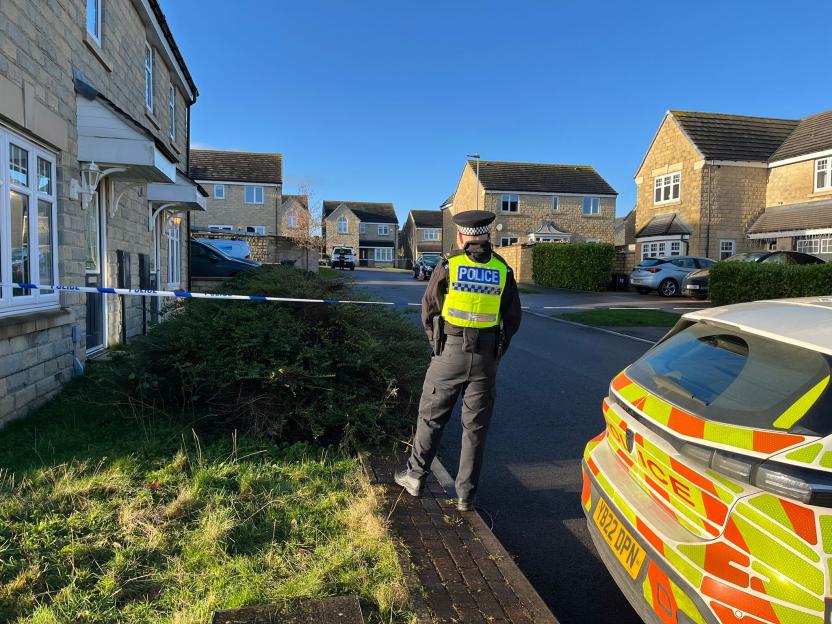 A police officer stands near police tape and a police vehicle in front of houses.