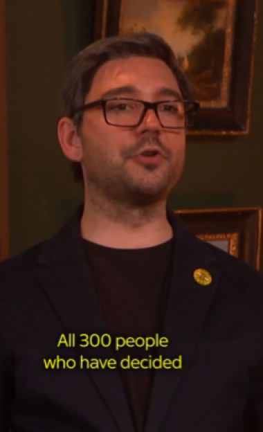 A man with glasses and a dark suit speaking, with the subtitle "All 300 people who have decided" on screen.