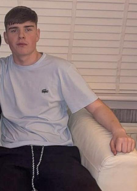 A young man, Kayden Moy, wearing a light blue t-shirt and dark pants, sits on a light-colored couch.