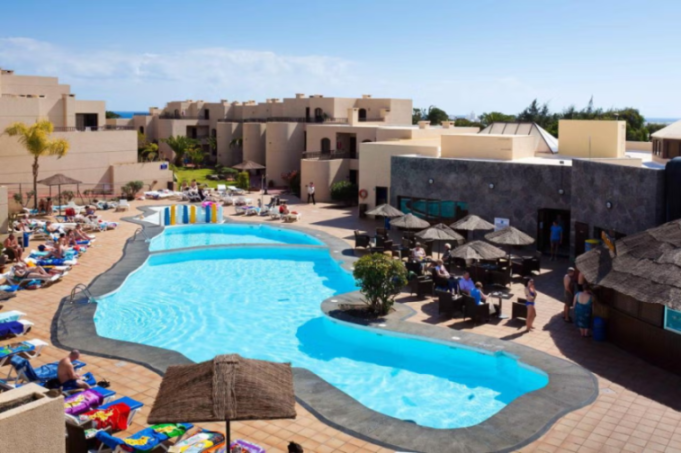 Elevated view of a resort pool area with buildings, sun loungers, and people relaxing.