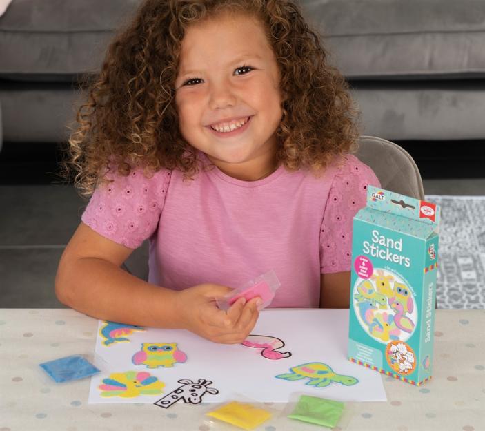 A smiling child creating sand stickers with a Galt Sand Stickers kit.