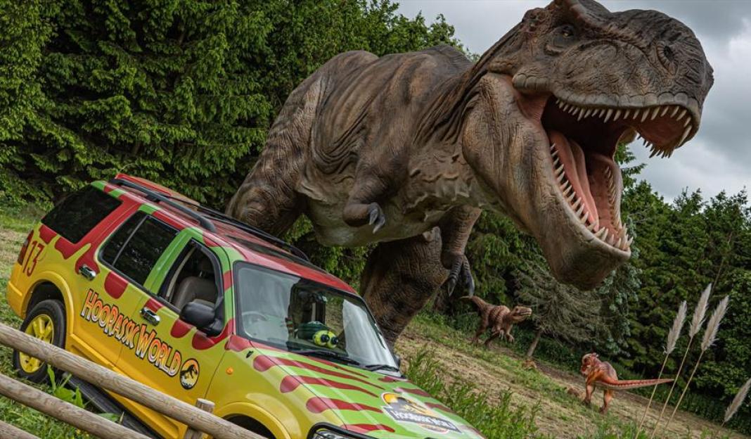 A Jurassic Park-themed vehicle with a large Tyrannosaurus Rex statue looming overhead.