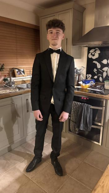 Lewis Walters in a black tuxedo with a bow tie, standing in a kitchen.