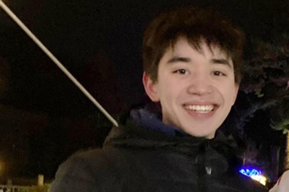 A young man with short, dark hair smiles at the camera, wearing a black puffer jacket.