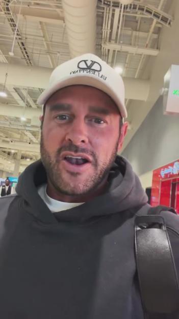 Lee Andrews in a white hat and black hoodie, speaking while standing in Dubai Terminal 2.