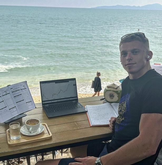Tom Roberts working at his business school in Thailand, with a laptop open on a table overlooking the ocean.