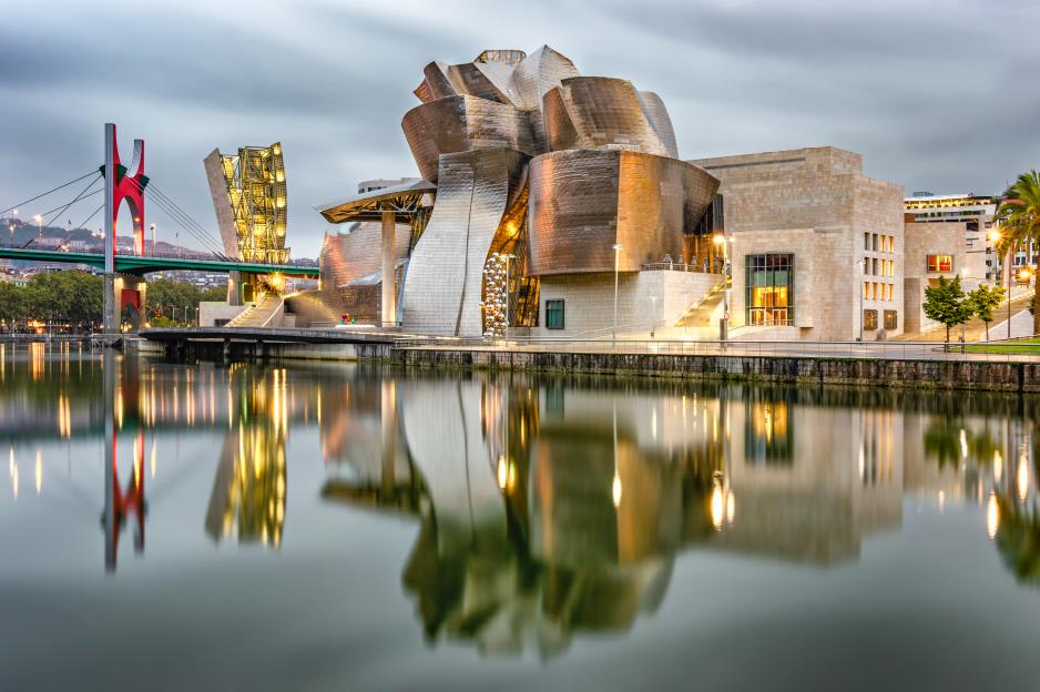 The Guggenheim Bilbao museum and La Salve bridge reflecting on the Nervion river at morning twilight.