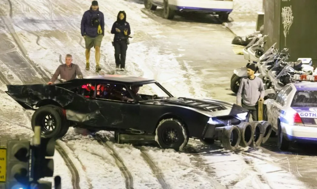 Batman filming on a snowy street, showing the Batmobile and crew members.