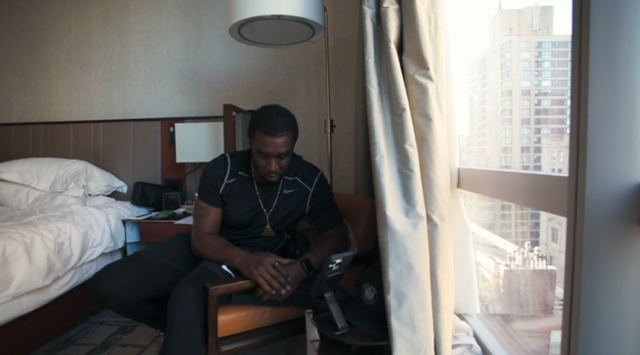 Sean Combs looks down while seated in a hotel room with a city view.