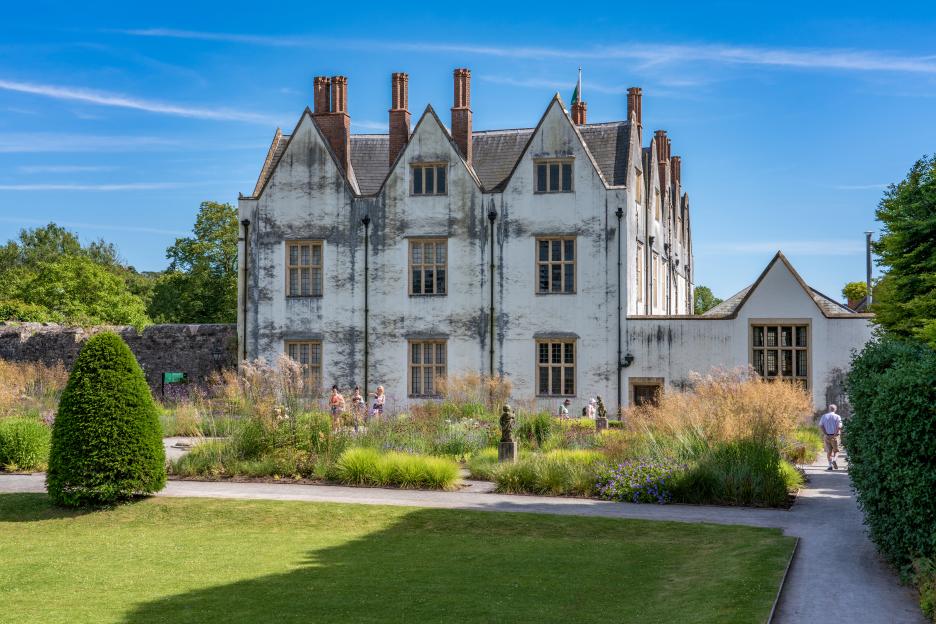 St Fagans Castle in Wales, a large white building with multiple gables and chimneys, surrounded by green lawns and flower gardens.