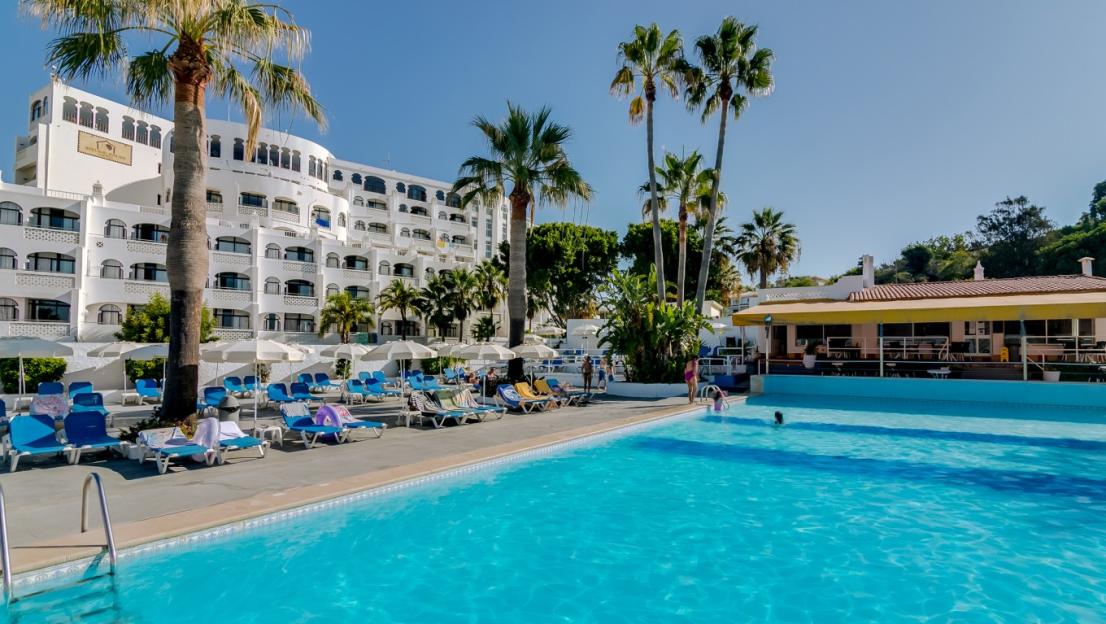 A hotel with a pool area filled with lounge chairs and palm trees.