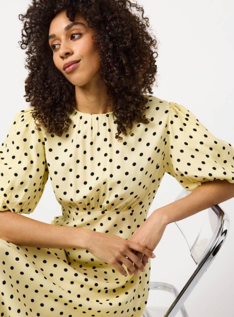 Woman with curly hair wearing a light yellow polka dot dress.