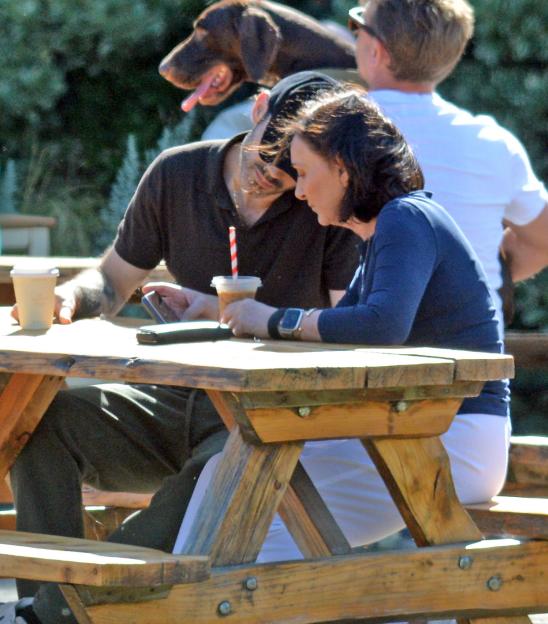 Shirley Ballas and Giuseppe Nonnis sitting at a picnic table with coffee, looking at a phone.