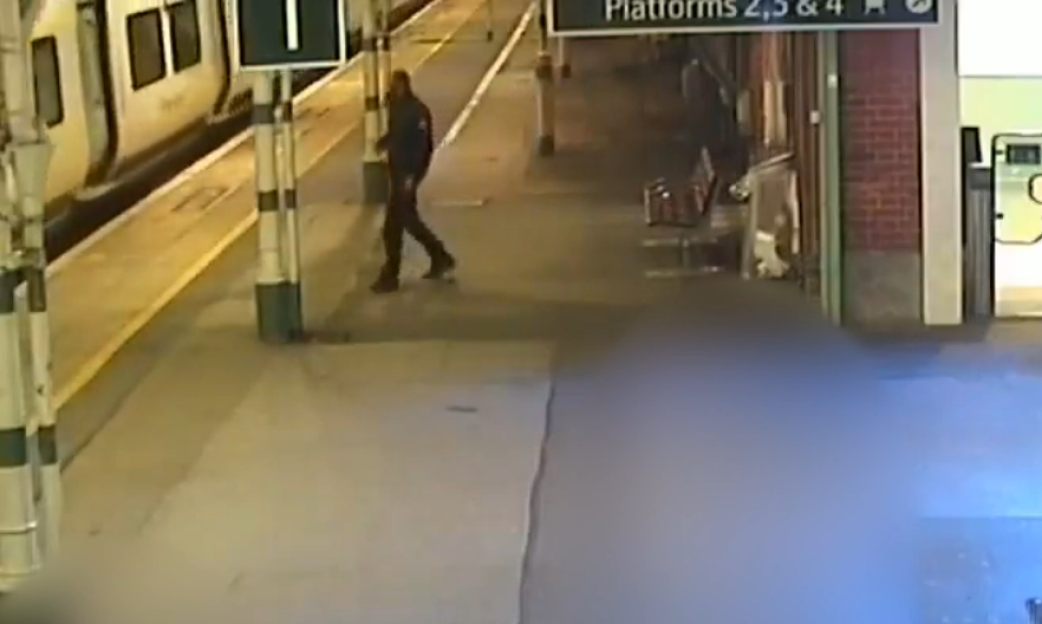 A man walks on a train platform with a train stopped at the platform.