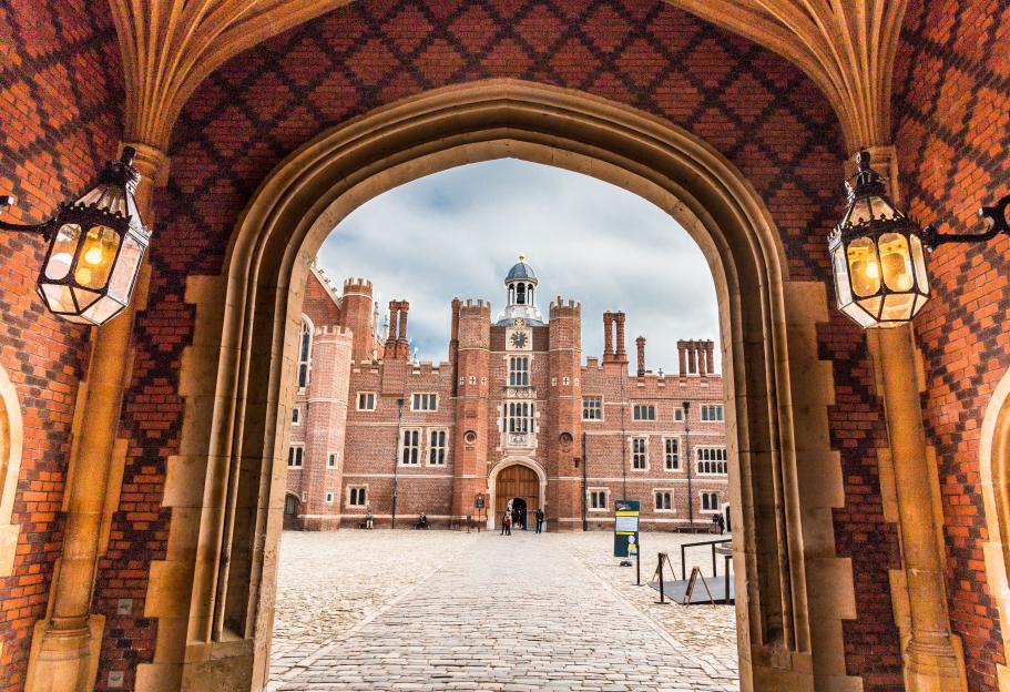 Hampton Court Palace viewed through a dark stone archway with two lanterns.