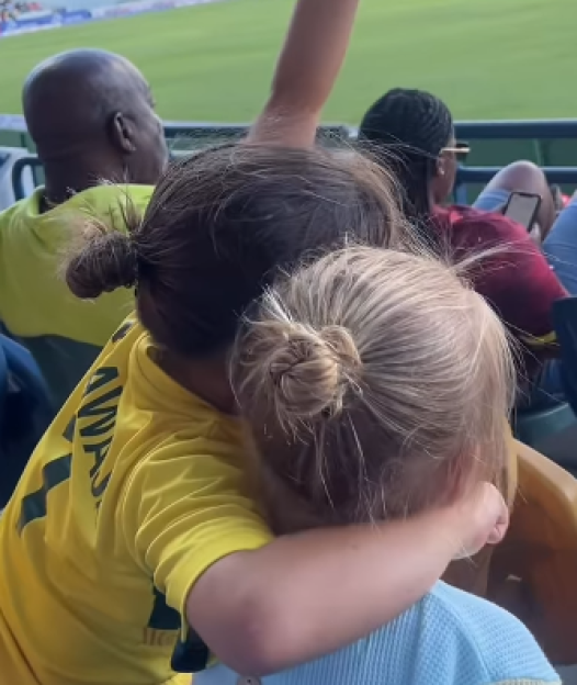 Two children hugging in stadium seats, seen from behind.