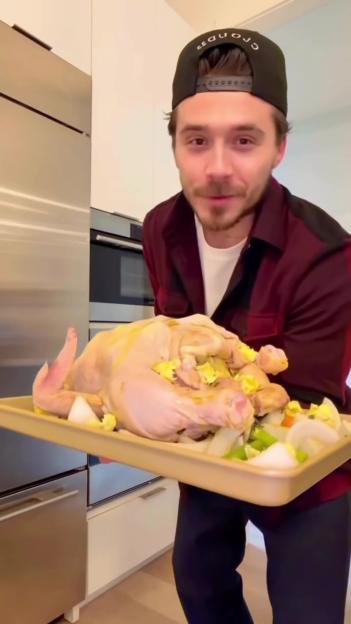 Man holding a raw turkey in a roasting pan with brine and vegetables.