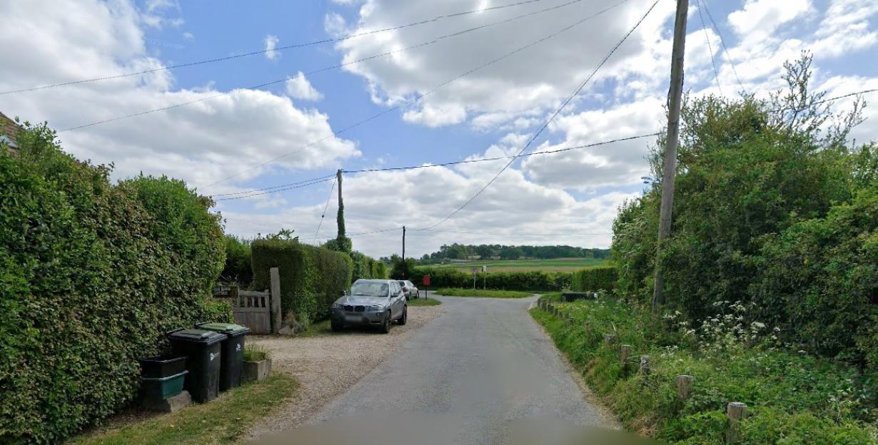 A rural road turning left, with a silver SUV parked on the left, and a red mailbox next to it.