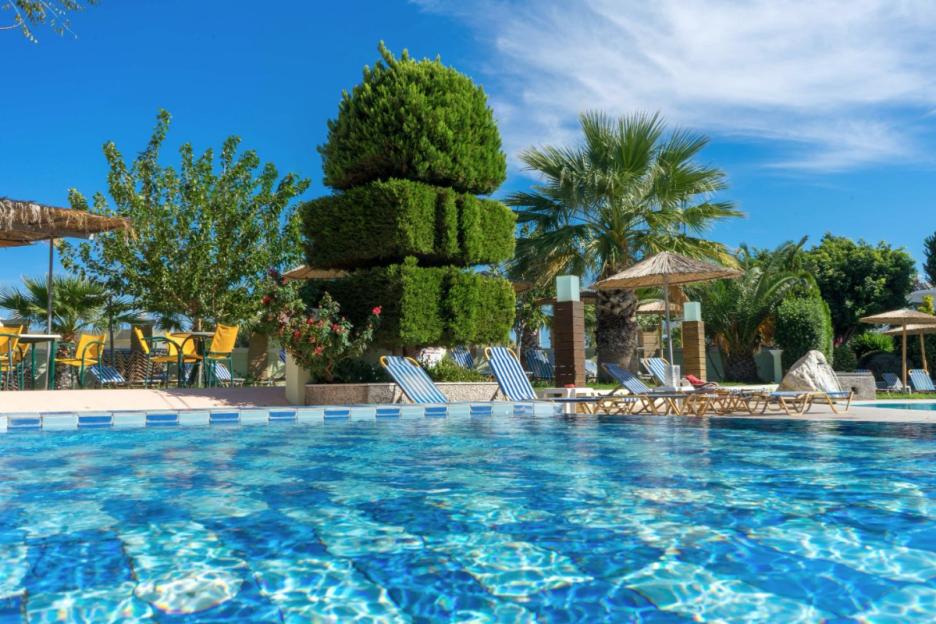 A swimming pool with sun loungers and straw umbrellas, surrounded by palm trees and other greenery.
