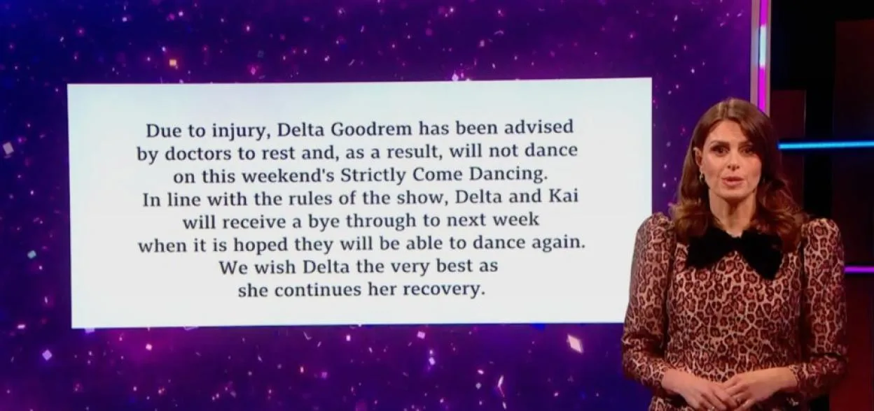 A television screen displays a message about Delta Goodrem's injury and upcoming absence from Strictly Come Dancing, while presenter Zoe Ball stands beside it.