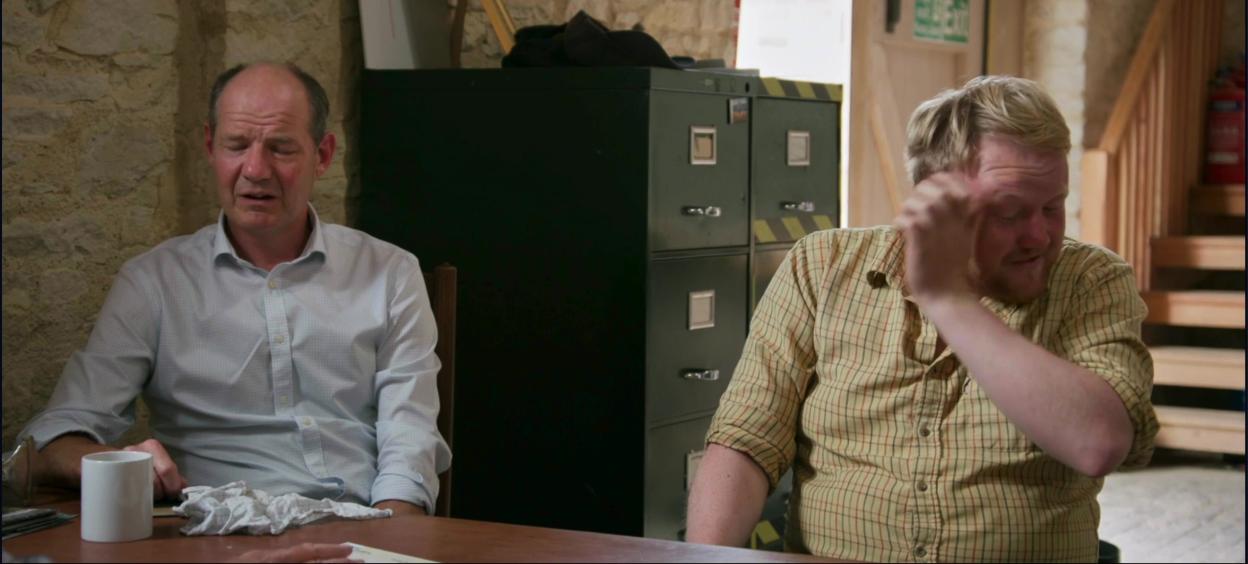 Two men seated at a table, one with tears in his eyes after being told of a cancer diagnosis.